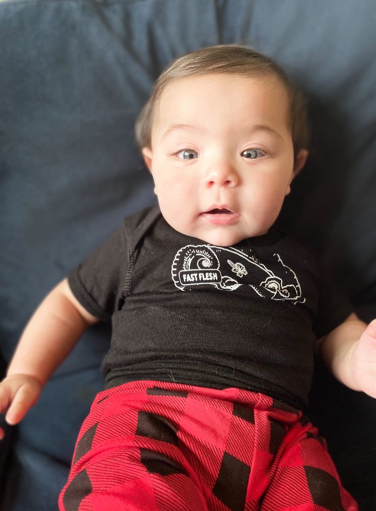 baby Miles in a Fast Flesh onesie and red flannel pants, looking very surprised by your submissions 