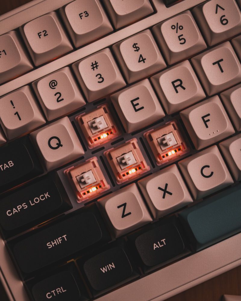 Close-up of a mechanical keyboard with beige keycaps and exposed switches glowing softly with orange backlighting.

