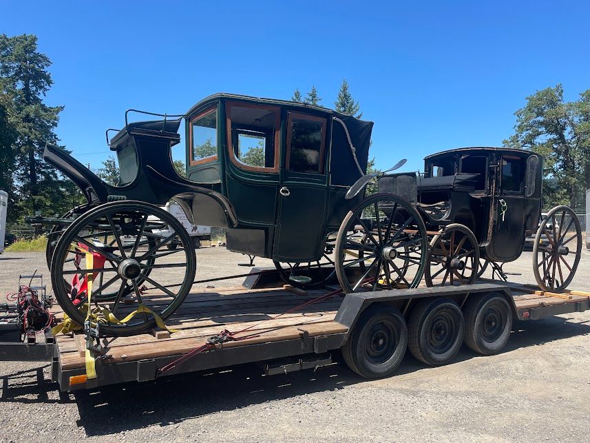 An ornate, dark green wagon and a smaller, simpler black wagon on a trailer bed.