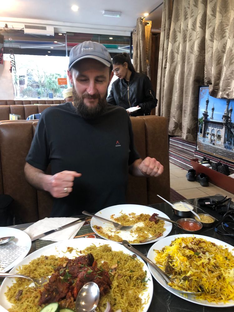 Luke Heslop sits at a table and excitedly tucks into the Mandi biriyani — yellow rice topped with meat — from the plates in front of him