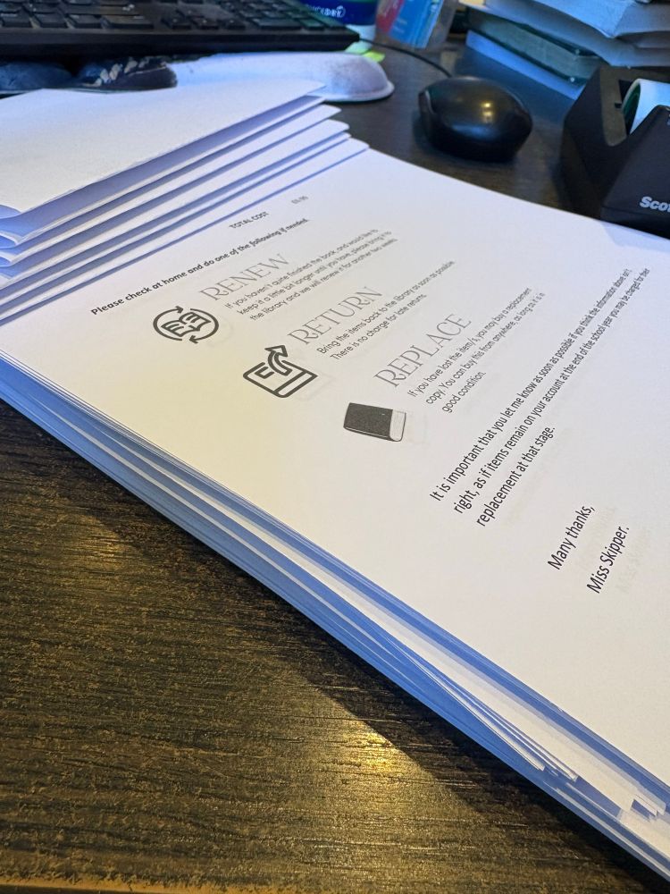 A photograph of a stack of notices for pupils alerting them to overdue books on their accounts. Some have already been folded ready for distribution.