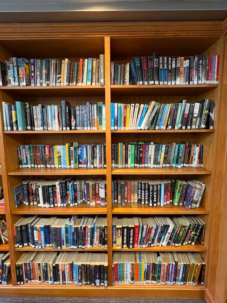A photograph of a section of a run of bookshelves. The shelves are full, and quite untidy.