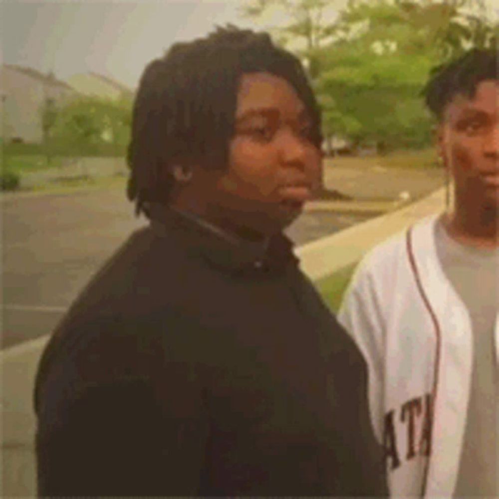 two men are standing next to each other on a sidewalk and one of them is wearing a baseball jersey .