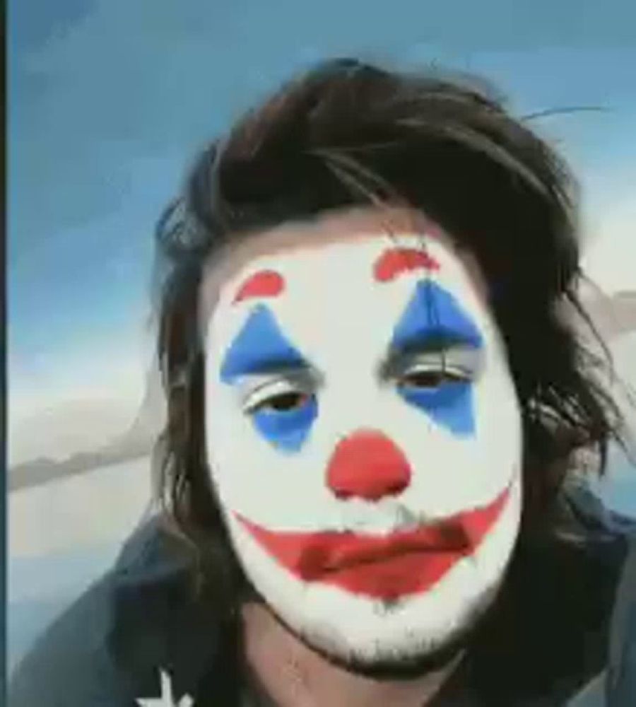 a man with long hair is wearing a clown mask on his face .