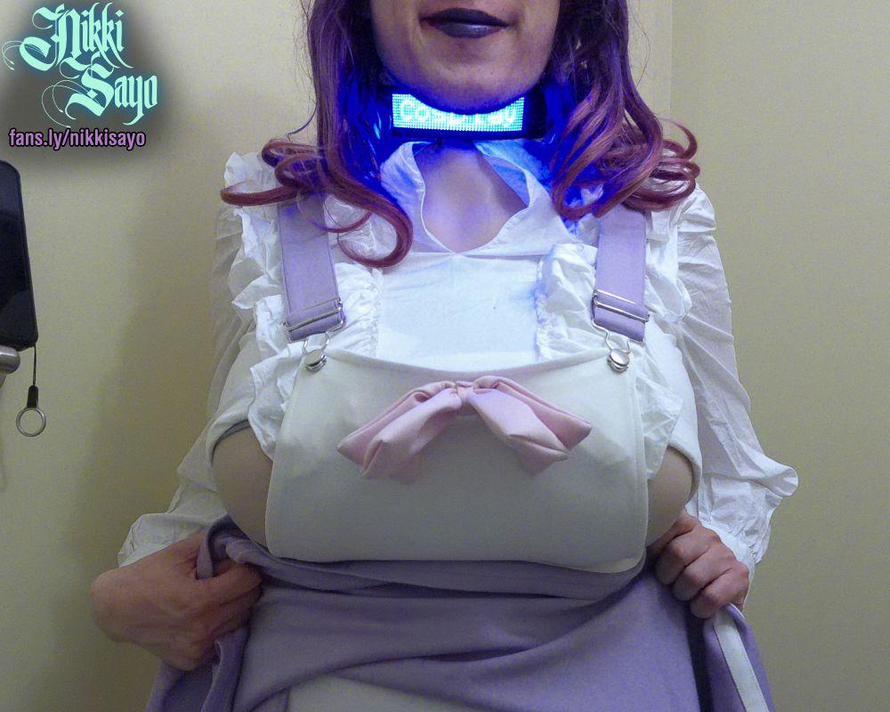 Purple haired femboy wearing a white/lavender skirtall as well as a frilly white long-sleeved crop top.