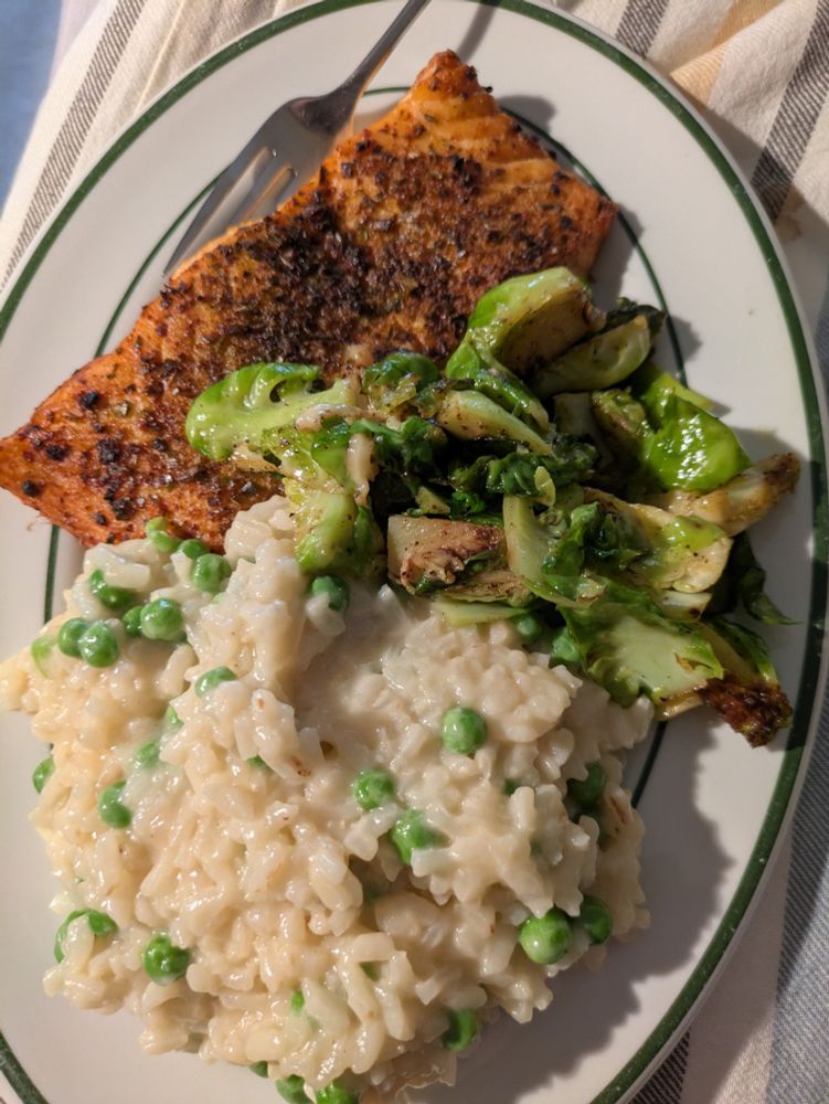 A plate with herb crusted salmon, sauteed brussel sprouts, and risotto with peas.