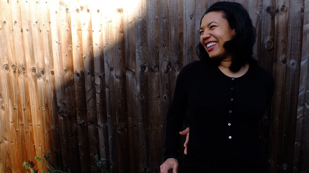 The poet Deanna Rodger, standing in front of a fence and smiling. 