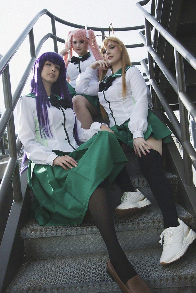 Group of Highschool of the Dead cosplayers in school uniforms sitting on metal staircase. Saya is on the highest step facing forward, Rei is on the next step down facing 3/4 to the left of frame, Saeko is on the bottom step facing 3/4 to the right of frame.