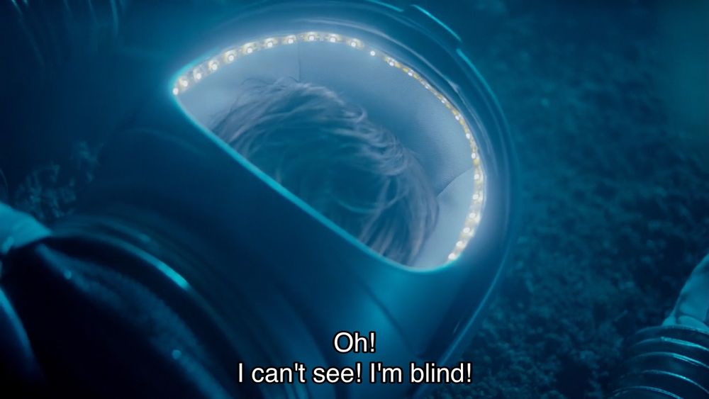 Matt Smith episode. The Doctor is laying on the ground, wearing a spacesuit. All you see inside is a fuzzy mess of hair — the back of his head. Caption reads, “Oh! I can’t see! I’m blind!” A woman is looking down at him, and says, “I think you've just got your helmet on backwards.”