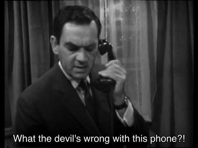 William Hartnell episode. A man in a business suit and tie is inside a room with nice gray curtains, holding a phone up to his ear. Caption reads, “What the devil’s wrong with this phone?!”