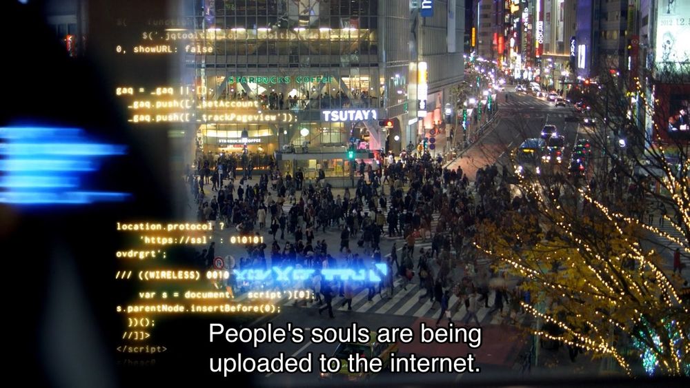 Matt Smith episode. Someone is doing a voiceover on stock footage of a bustling city corner at night, bright shop lights, headlights, Christmas lights, with glowing yellow code on the left side of the screen, like some hacker movie. The voiceover is coming from a pixelated webcam video of a young man in a jumper sitting in front of a bookshelf with Things on it, talking directly to camera. Captions read, “People’s souls are being uploaded to the internet. Sometimes you can hear their screams.”