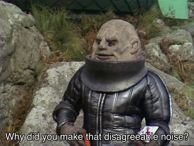 Tom Baker episode. (Aren’t they all?) A Sontaran, an ugly potato head man in a shiny polyester uniform with the helmet removed, is standing in a quarry. They’re putting a gun back in their holster, looking at Sarah Jane just off screen. Caption reads, “Why did you make that disagreeable noise?”