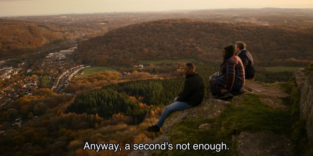Jodie Whittaker episode. Ryan, Graham and Grace are sitting on a cliffside, overlooking Sheffield. The sun is setting. It’s very picturesque. Caption reads, “Anyway, a second’s not enough.”
