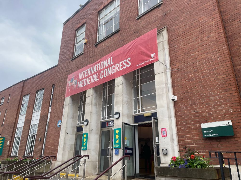 A red banner indicating the presence of the International Medieval Congress hung over the white bring entrance of a red brick building.  