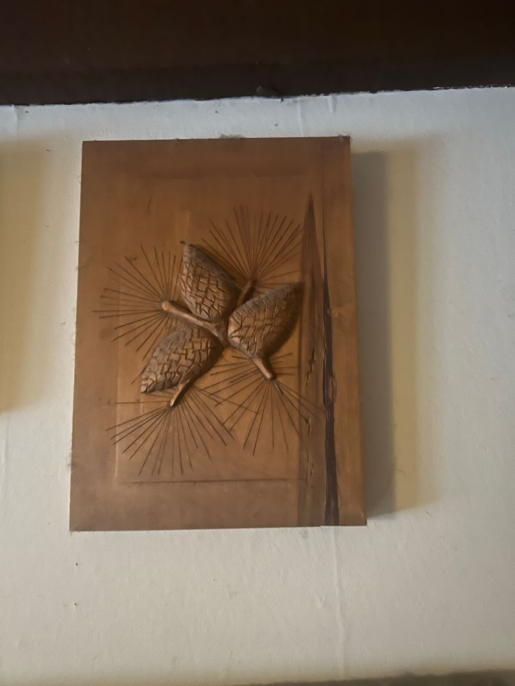 a relief carving of pine cones and pine needles on a knot streaked block of wood. 