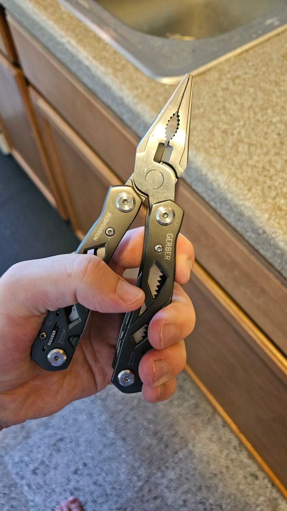 A hand holding the grey pair of pliers that would be the drain stop's demise