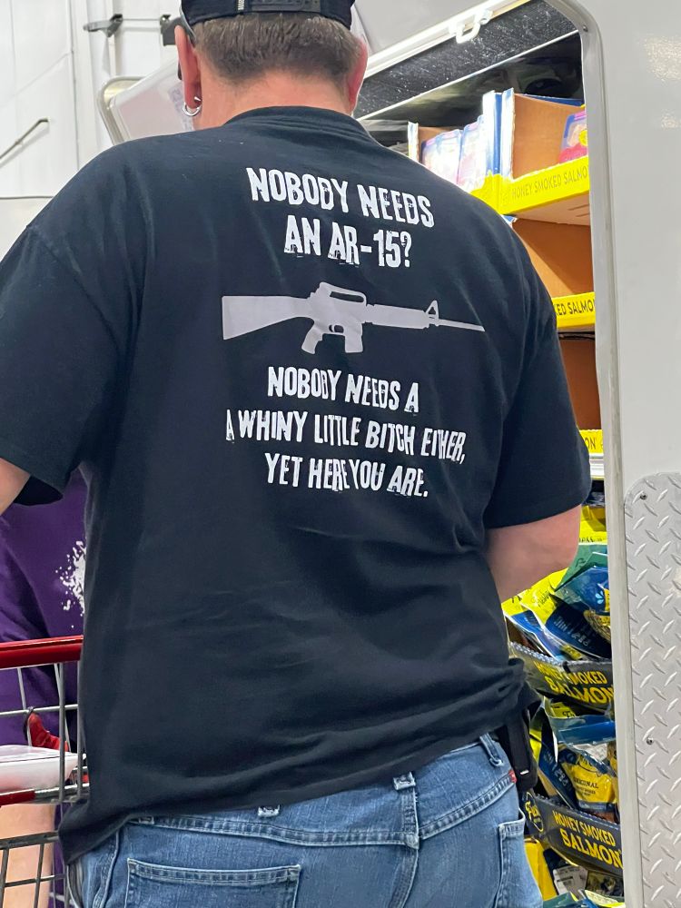 A guy wearing a t shirt that says on the back, NOBOBY NEEDS AN AR-15? NOBODY NEEDS A WHINY LITLE BITCH, YET HERE YOU ARE.