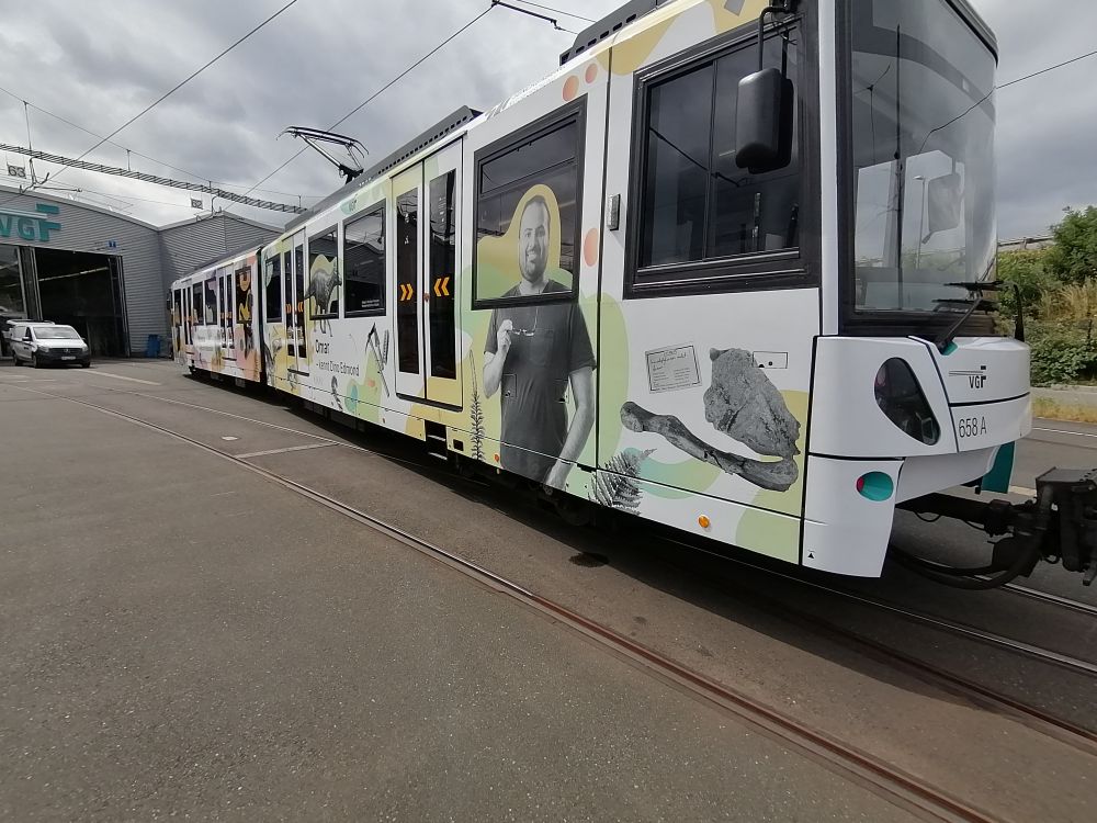 A photo of a U-Bahn carriage in Frankfurt that has been decorated with a loose collage of specimens and labels to advertise the museum. A photo of me is on the side, my head printed on the window. The photo is black and white and I am holding my glasses on the right hand.

---

Una foto de un vagón de metro en Fráncfort, decorado con un collage de especímenes y etiquetas para anunciar el museo. Una foto mía está impresa en un lateral, mi cabeza, en la ventana. La foto es en blanco y negro y sostengo mis lentes en la mano derecha.