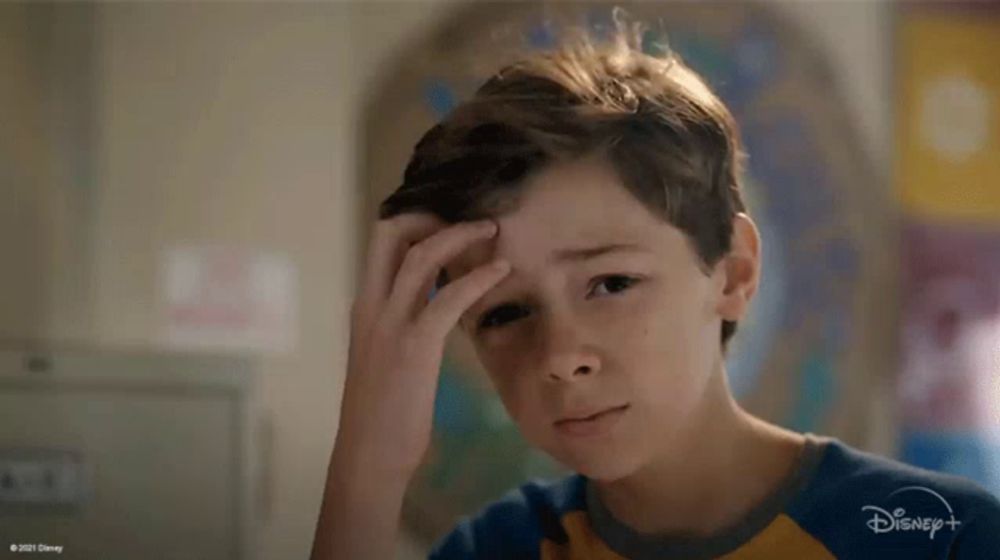 a young boy is sitting in front of a map and looking at the camera with a sad look on his face .