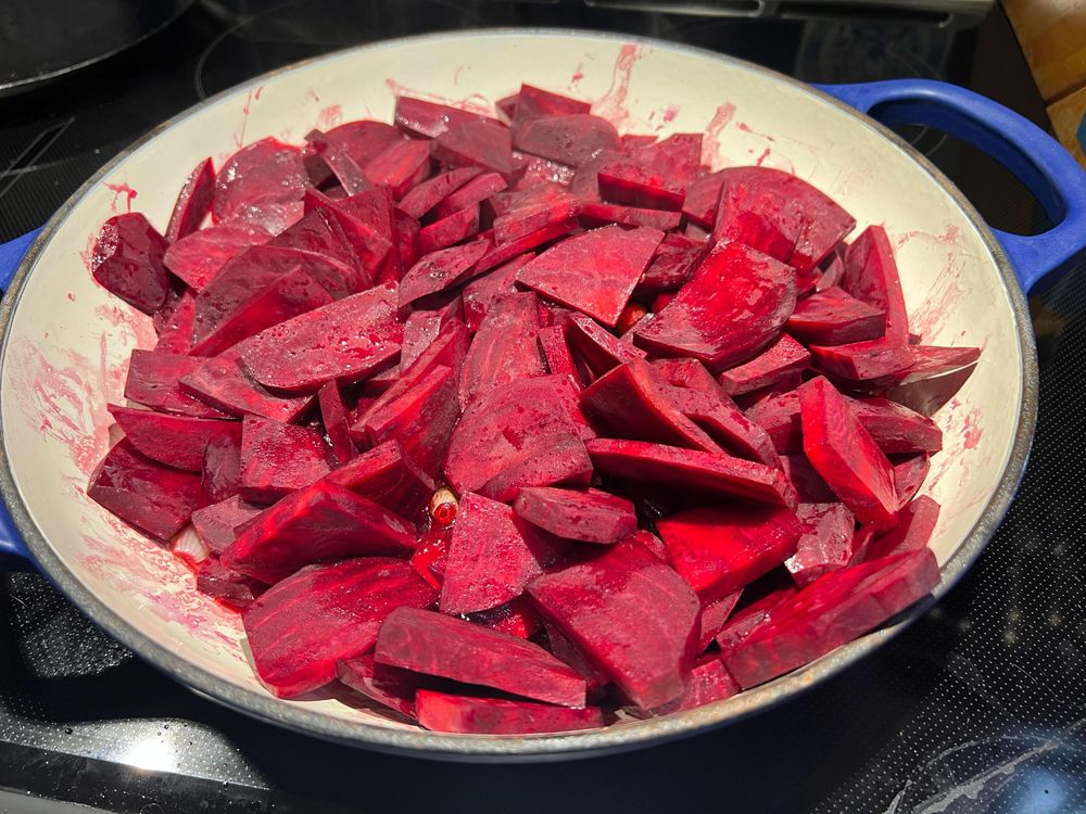 A large, blue and yellow pan with sliced red beets cooking in it, on top of an electric stovetop.