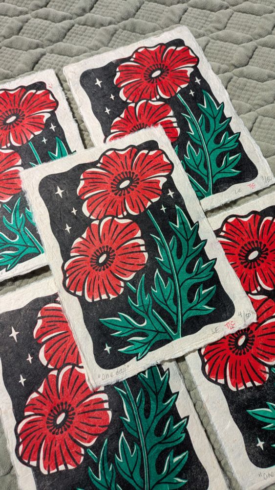 A hand-printed design of two poppies growing against a starry black sky. The poppies are bright red, with little details to show the texture of the petals. The stems and leaves grow up around them in a grassy green that looks darker and lighter in different areas. There's pops of highlight throughout, brightening the composition. It's one print overlaid on a grid of four.