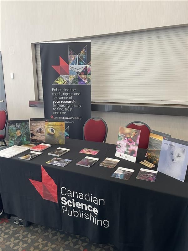 Booth at conference for Canadian Science Publishing. Branded black tablecloth with coloured postcards in front of a vertical banner