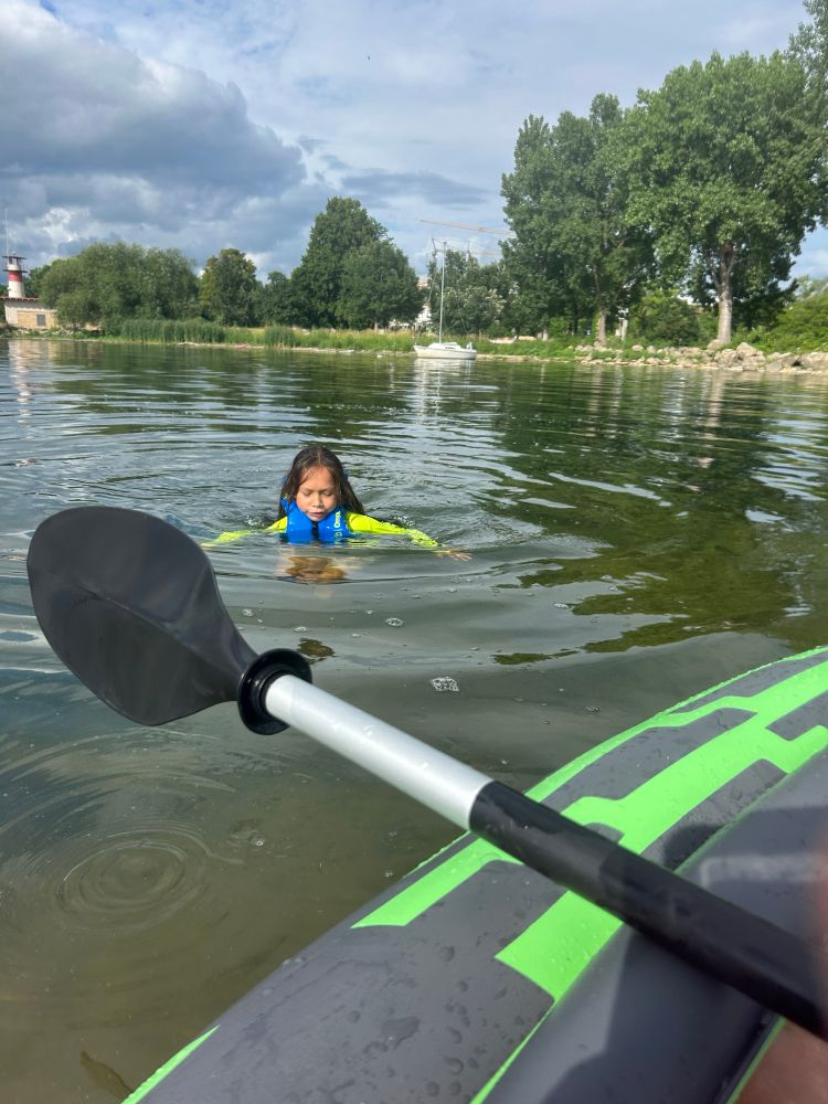 Young boy swimming in lake with PFD on