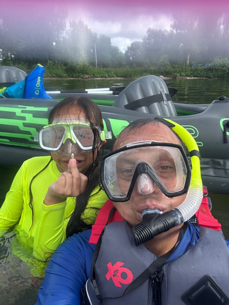 Man and his son in lake wearing their snorkeling gear with son holding up a shell