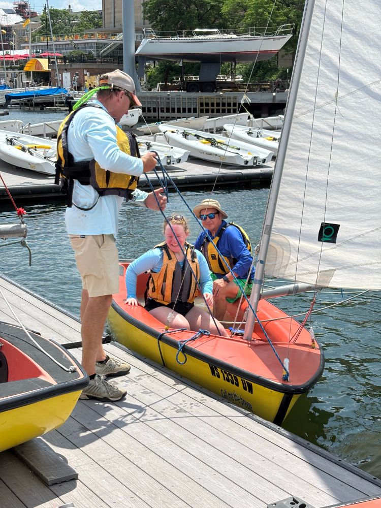 Man pulling the bow line of a small dinghy sailboat carrying another man and woman inside.