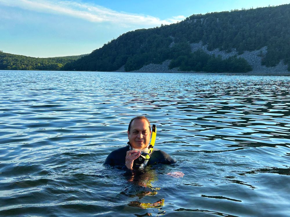 Man floating in lake wearing wetsuit and holding a snorkel mask and snorkel