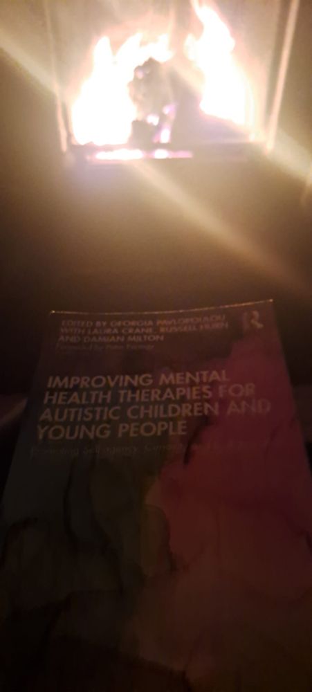 Picture of book in front of an open fire. Booked called "Improving MH therapies for autistic children and young people"