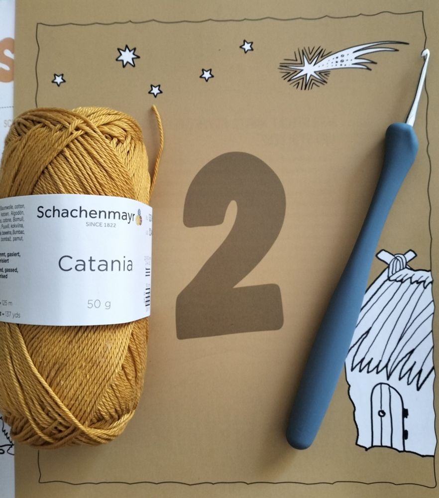 Seite 2 des Wollowbies Adventskalender, darauf liegen eine Häkelnadel und ein Knäuel Schachenmayr Catania in Sand