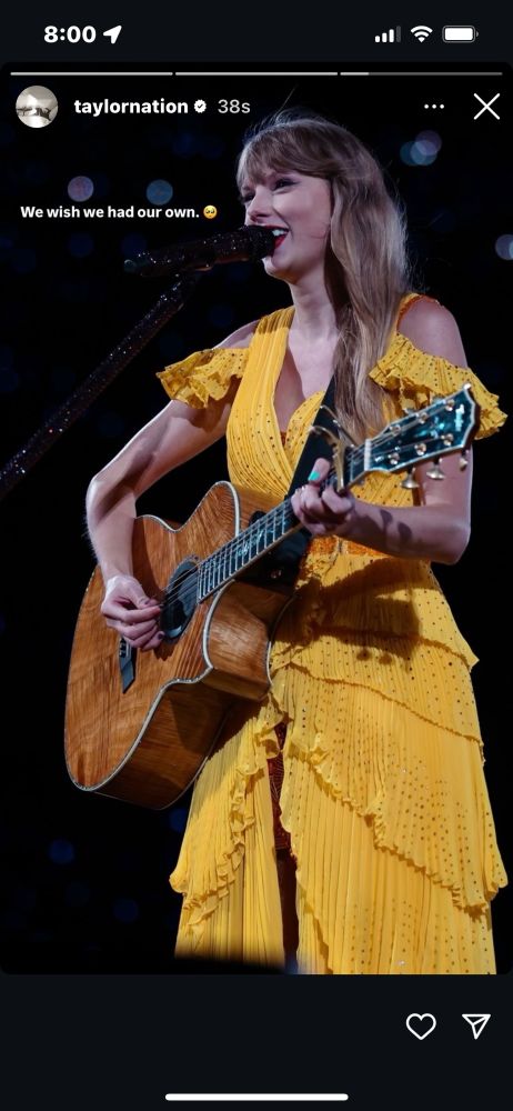 taylor swift with a guitar in a yellow dress during surprise songs at the eras tour. caption by taylor nation says “we wish we had our own”