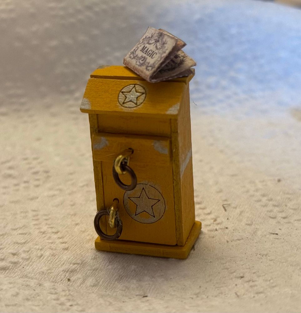 a magical yellow cabinet with silver painted stars and detailing that i kind of fucked up, with gold and brown hardware and a little paper book resting on top that says magic on the outside. you can't see the fucked up glue on it in this picture but trust me it's there too