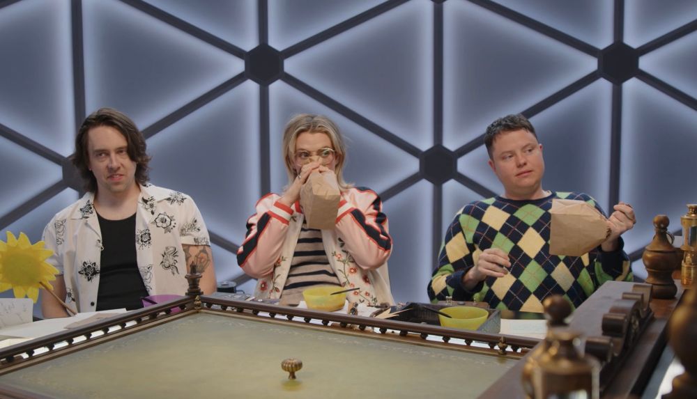 murph holding a sunflower wand, siobhan blowing into a paper bag, and ally holding a bag full of air in preparation to pop it as off-screen brennan attempts to guide the adventuring party back on track