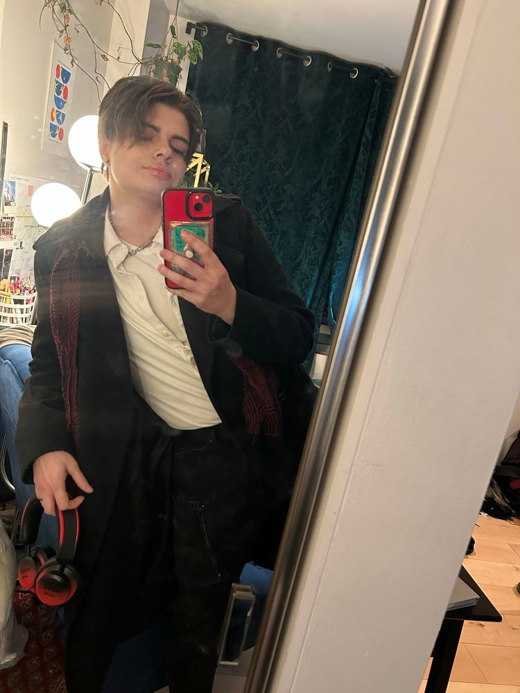Mirror selfie with mocking wearing a black overcoat over a white button up and a red scarf