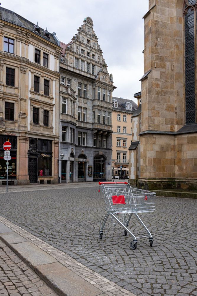 Ein herrenloser Einkaufswagen auf der Straße vor einer Kirche. Im Hintergrund sind Altbauten zu sehen.