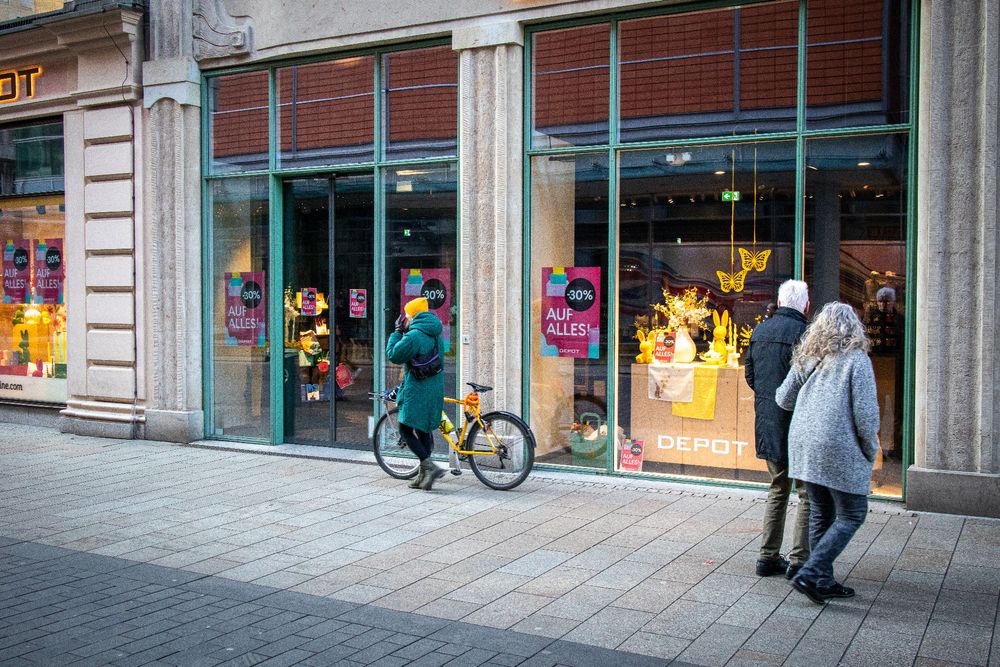 Eine Frau mit gelber Mütze und gelbem Fahrrad vor einem Schaufenster mit gelben Artikeln in der Auslage.