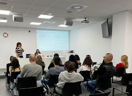 En aquesta fotografia, agafada des del darrera, es poden veure els professionals de Support (d'esquenes) escoltant a la Maribel i la Raquel, professionals de l'Entitat que coneixen els circuits d'ajudes.