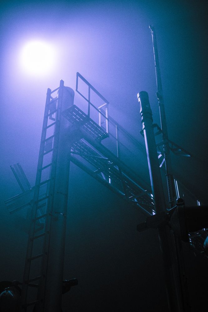 A bright light glows behind a railroad crossing signal, its rays illuminating dense fog that surrounds everything. 
