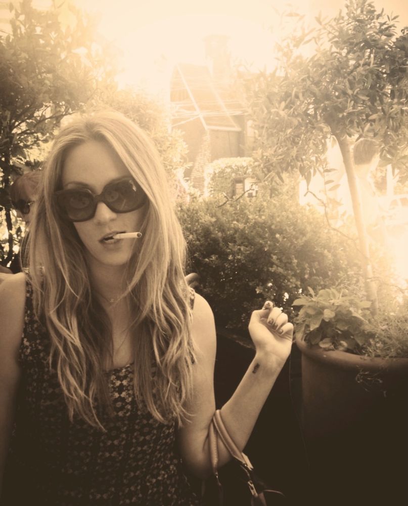 A blonde girl with a cigarette in her mouth looking cool as hell 