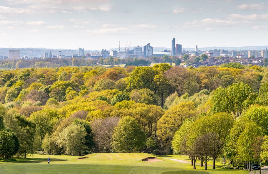 A skyline image of Leeds in which the city centre can be seen in the far distance, with a park filled with trees in the foreground. 