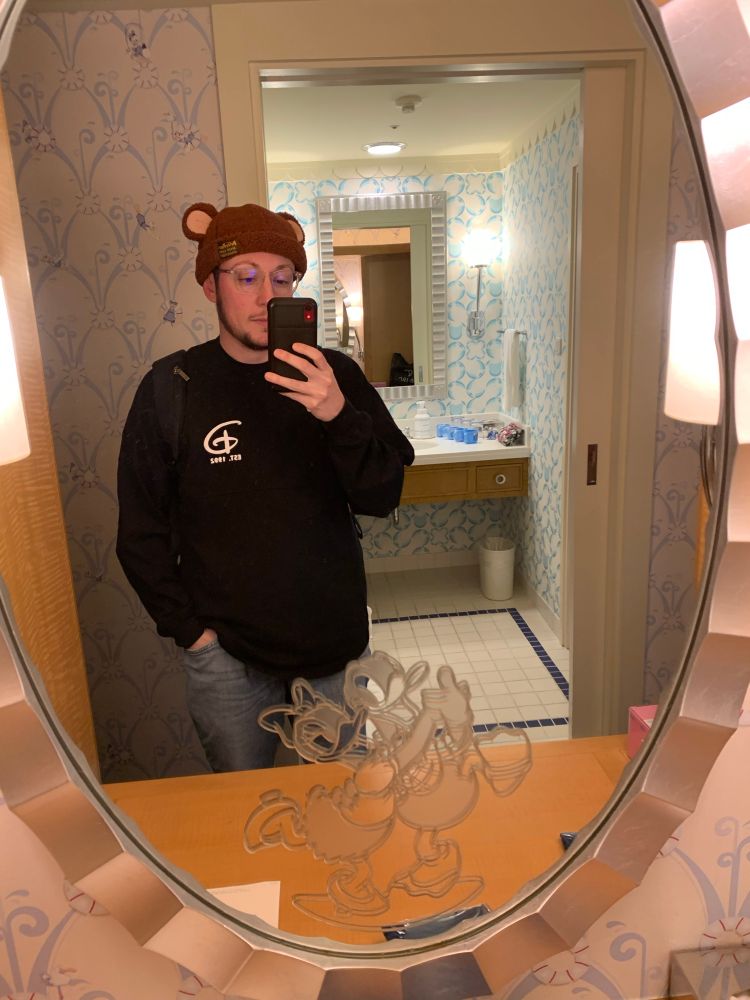 Ben taking a mirror selfie in the Disney Ambassador hotel in Tokyo, wearing a brown bear hat and a black Disneyland Paris long sleeve shirt. (Face reveal!!!)