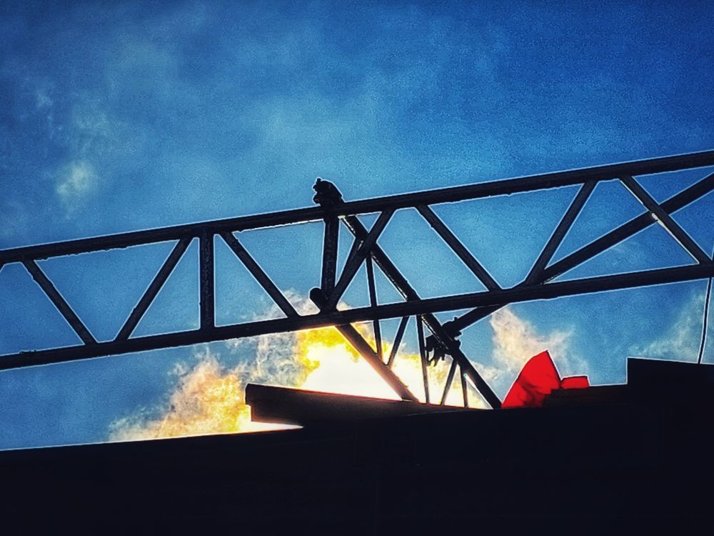 Dachtraverse mit zwei roten Plastikzipfeln vor blauem Himmel mit Sonne.