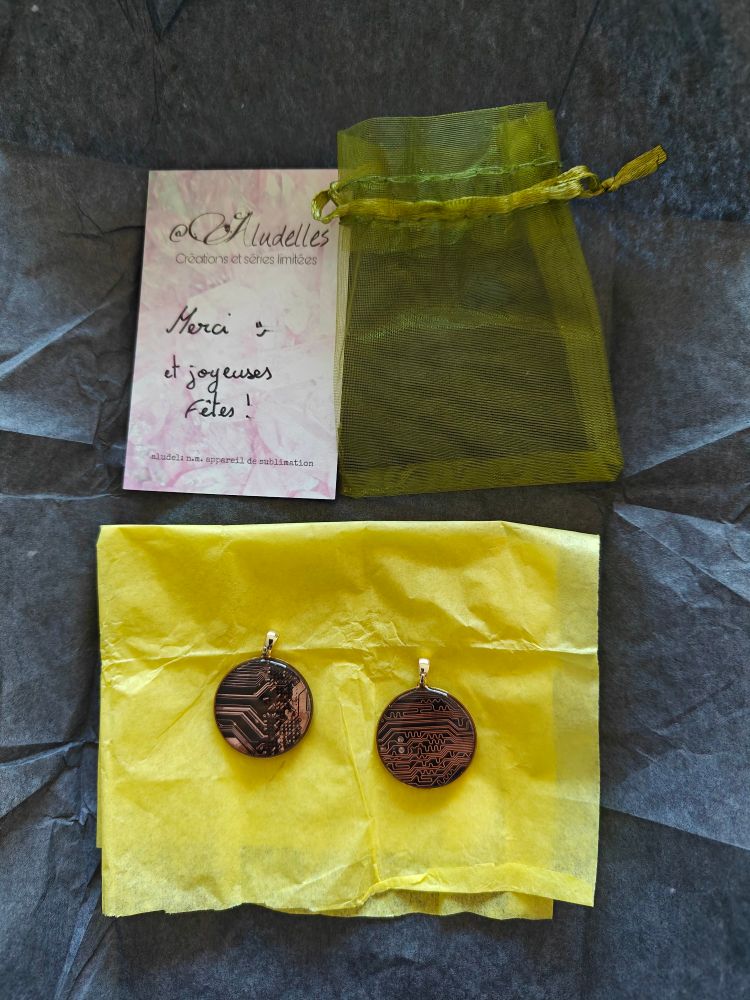 2 magnifiques médailles
Carte mère noire coulée dans de la résine
Posée sur papier de soie jaune
Lui-même sur papier de soie noir
Au dessus une petite pochette transparente jaune
Et une carte de visite de Aludelles sur laquelle est écrit à la main
Merci et joyeuses fêtes
