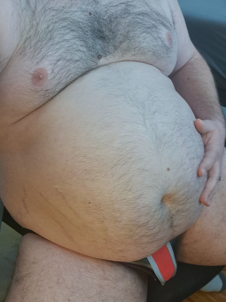 A fat man in a jockstrap grabs his belly.
