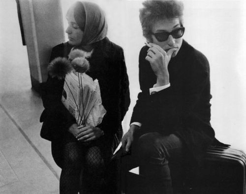 Joan Baez and Bob Dylan sitting down on suitcases