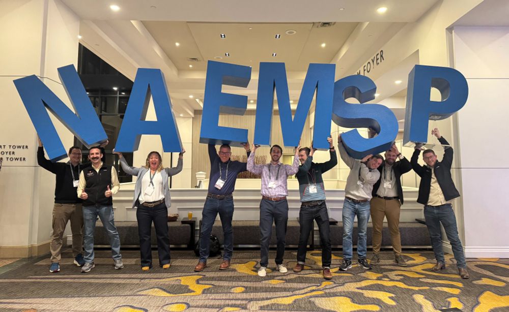 People stand indoors holding up large letters spelling out N-A-E-M-S-P.