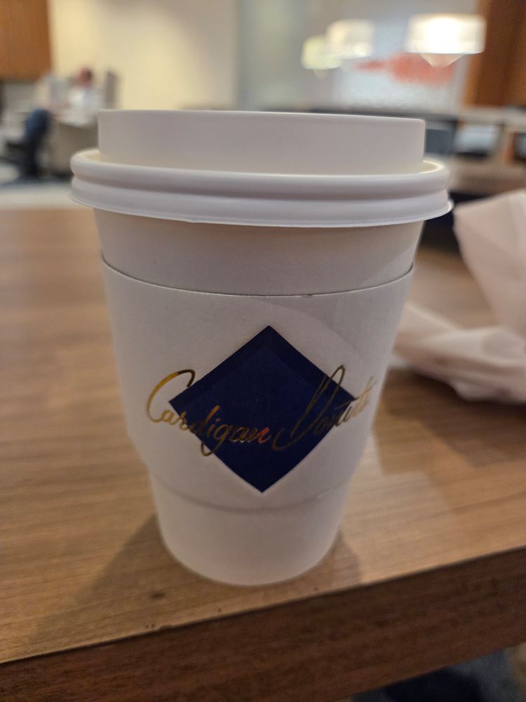 Shot of a cup of a to-go cup of tea with a cardboard Cardigan Donut diamond logo jacket. This cup of tea is the golden milk latte - the turmeric in this blend is soothing to my seasonal allergies. 