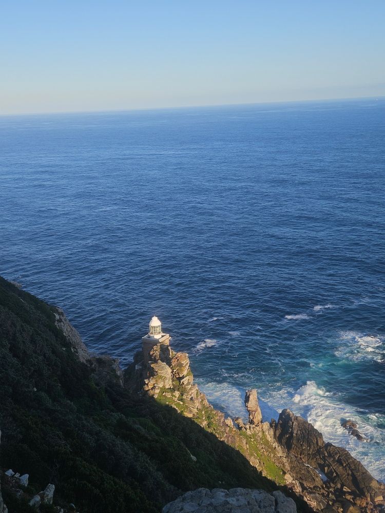a small white lighthouse on a rocky outcrop in the foreground, the ocean in the background 